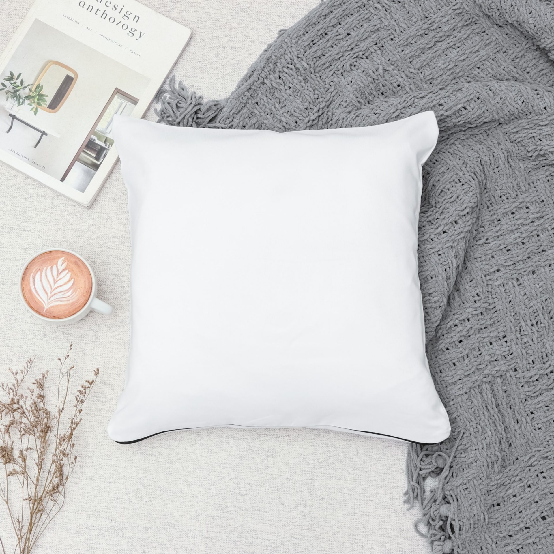 Grey throw blanket and white pillow on cream colored floor rug